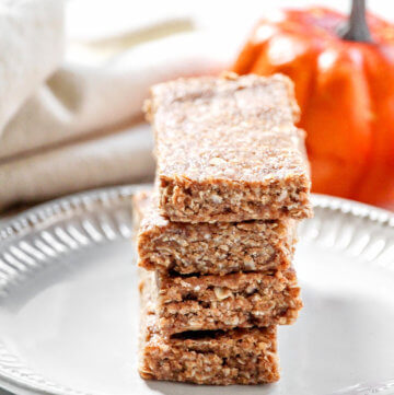Vertical image of a stack of four Gluten-Free Vegan No-Bake Pumpkin Spice Granola Bars on a small grey plate with a cloth napkin and small pumpkins in the background