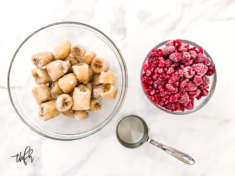 Overhead image of two glass bowls filled with frozen bananas and frozen raspberries