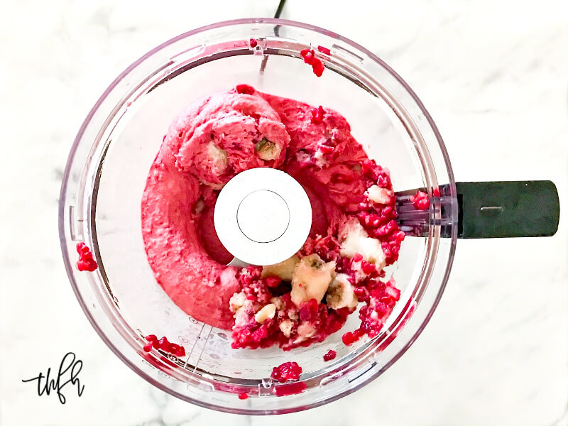 Overhead image of frozen bananas and frozen raspberries partially blended in a food processor