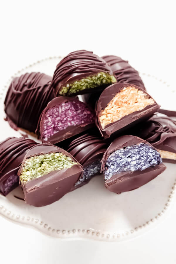 Vertical image of multiple chocolate covered colored coconut eggs on a decorative white platter on a solid white background