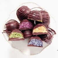 Multiple pieces of chocolate covered colored coconut eggs on a decorative white platter on a solid white background