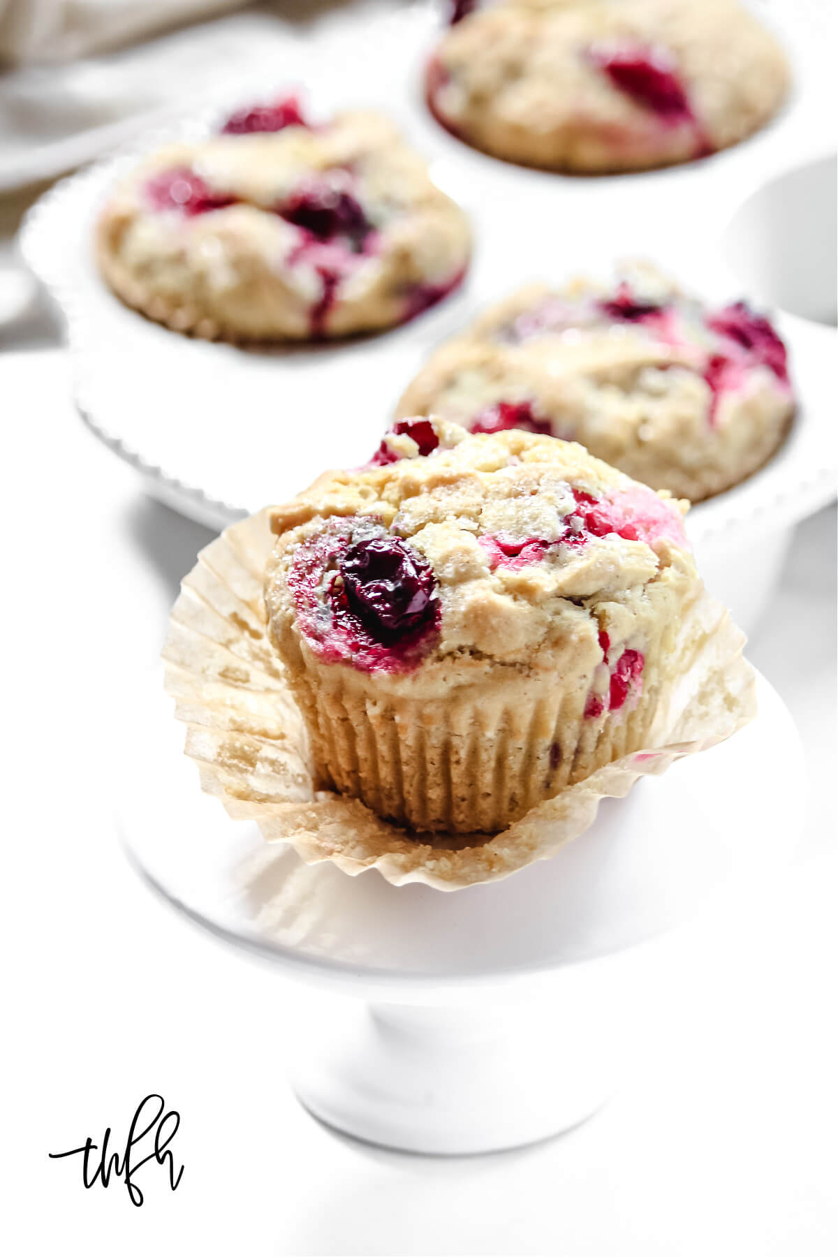 Close up vertical image of a cranberry orange muffin on top of a small white pedastal
