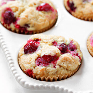 Close up vertical image of a cranberry orange muffin in a decorative white muffin pan