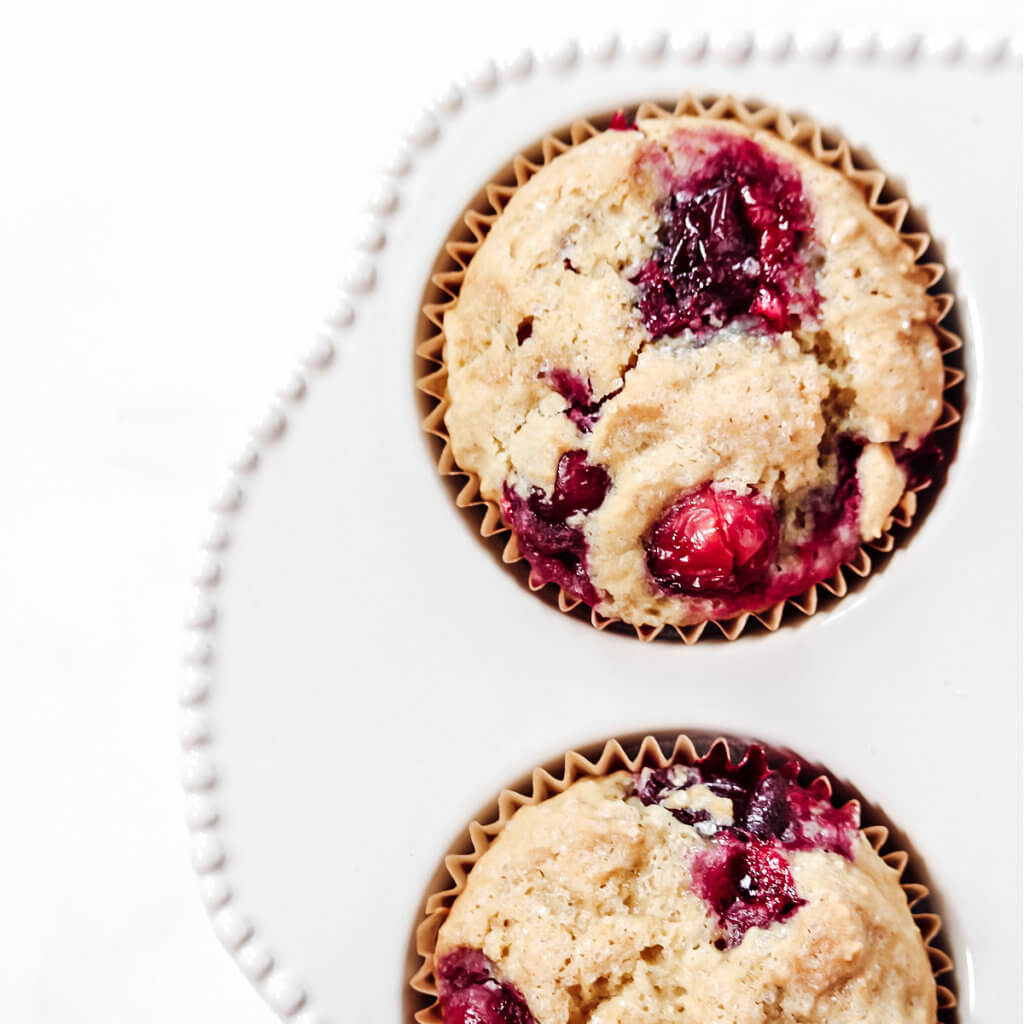 Overhead image of two cranberry orange muffins in a decorative white muffin tray