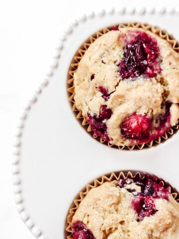 Overhead image of two cranberry orange muffins in a decorative white muffin tray