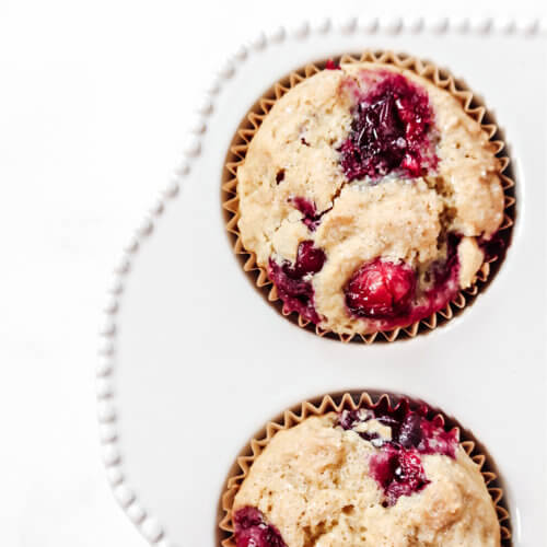 Overhead image of two cranberry orange muffins in a decorative white muffin tray