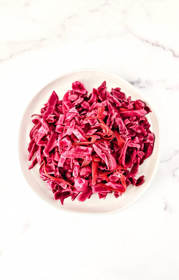 Overhead image of pickled red cabbage on a white plate on a white marble background.