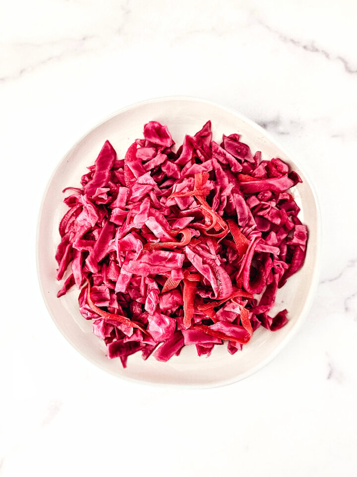 Overhead image of pickled red cabbage on a white plate on a white marble background.