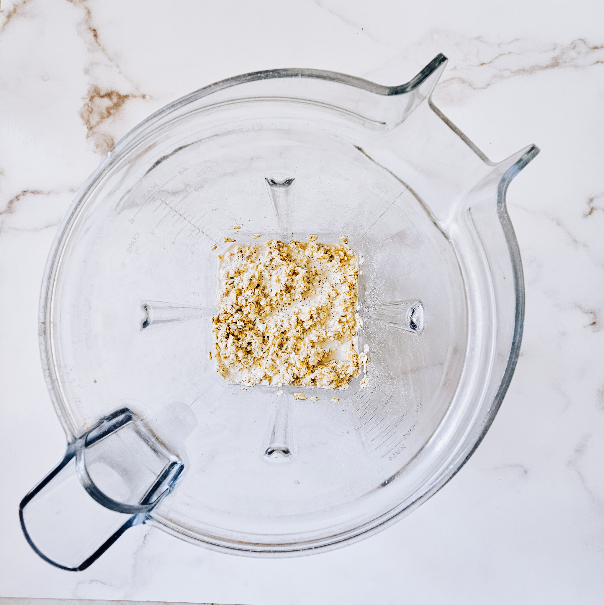 Overhead image of Ingredients needed to make gluten-free vegan oat tortillas soaking in a Vitamix blender on a white marble surface.