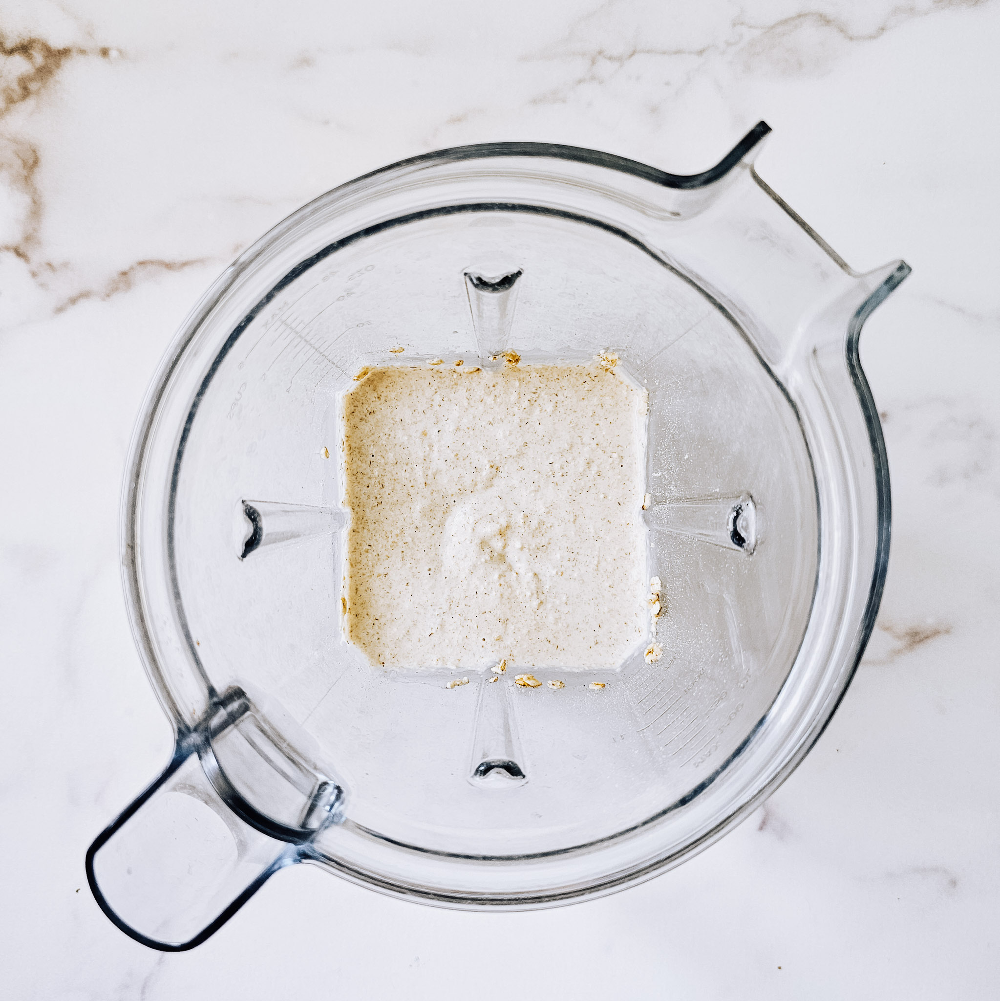 Overhead image of ingredients needed to make gluten-free vegan oat tortillas mixed together in a Vitamix blender on a white marble surface.