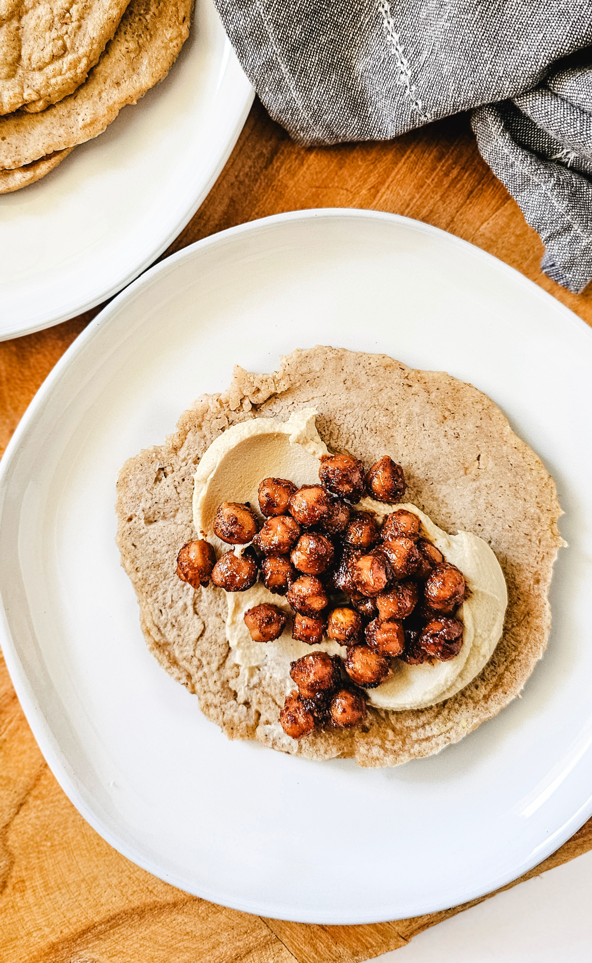 tortilla with hummus and chickpeas gluten-free vegan oat tortilla with hummus and seasoned chickpeas on a white plate on a wooden surface.