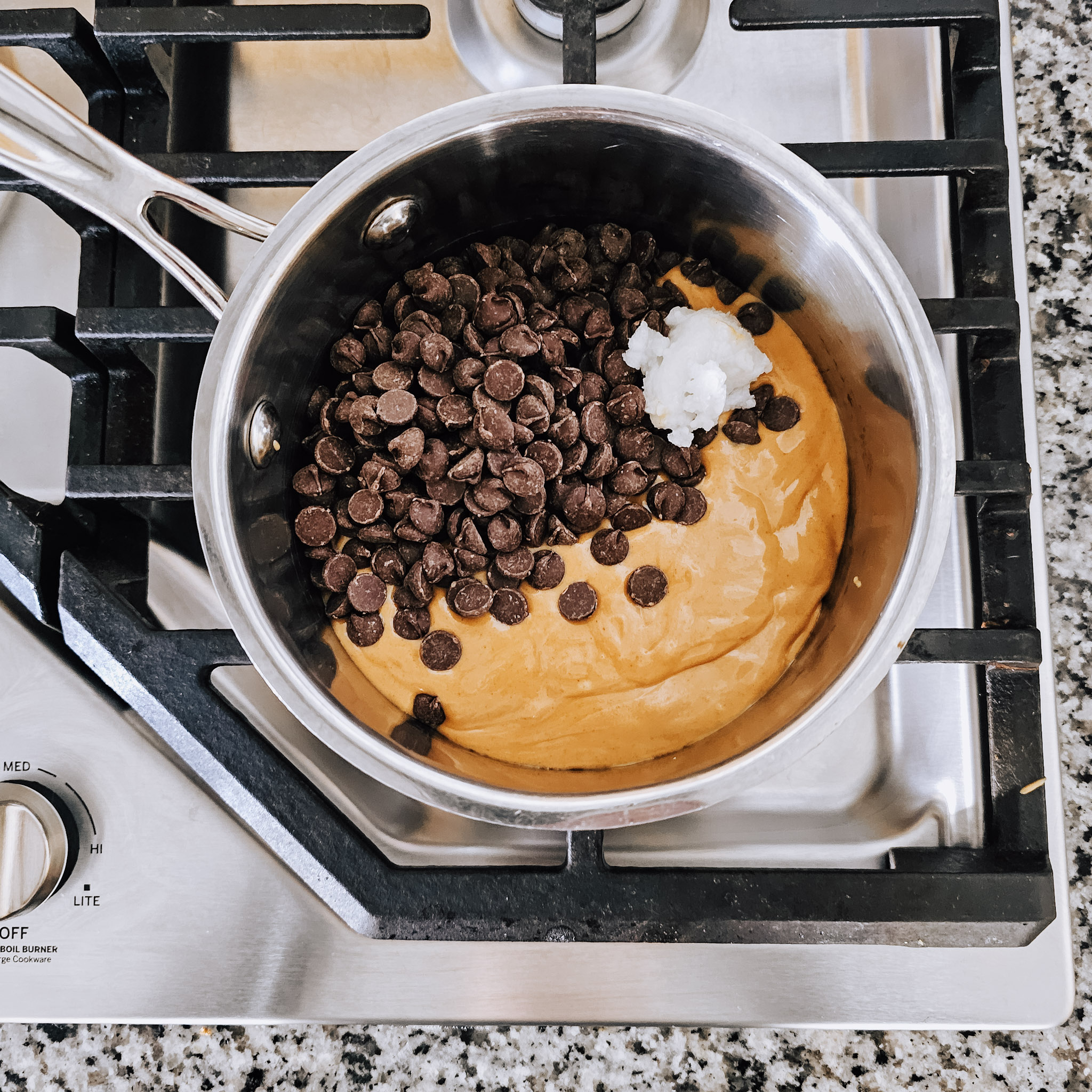 Overhead image of the ingredients needed to make the middle layer of gluten-free vegan no-bake chocolate peanut butter oat bars in a stainless steel saucepan on a gas cooktop.