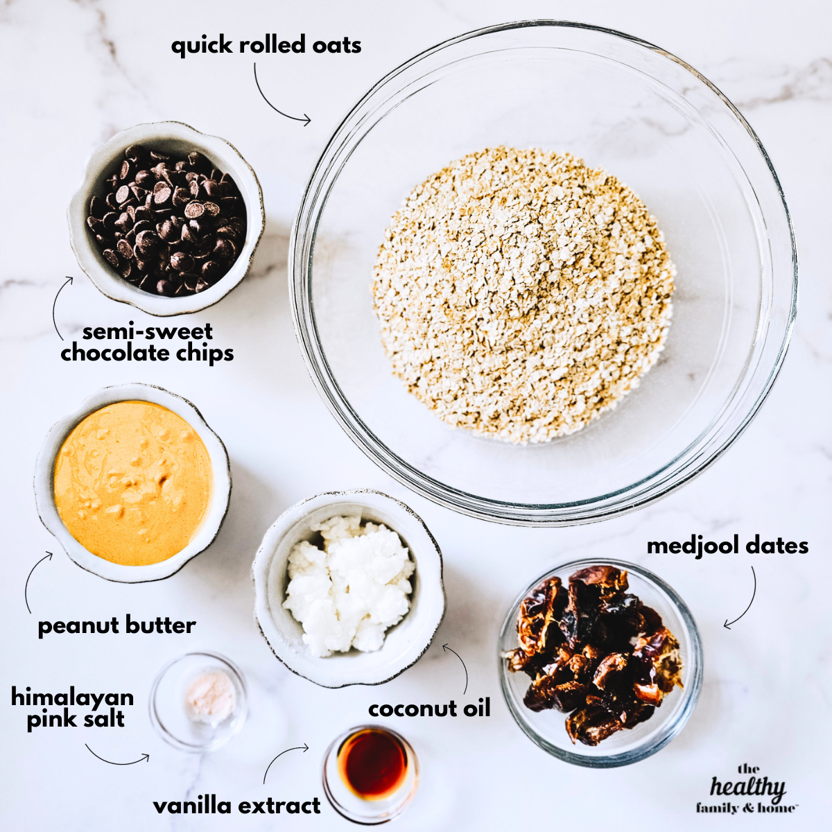 Overhead image of labeled ingredients needed to make gluten-free vegan no-bake chocolate peanut butter oat bars in small bowls on a white marble surface.