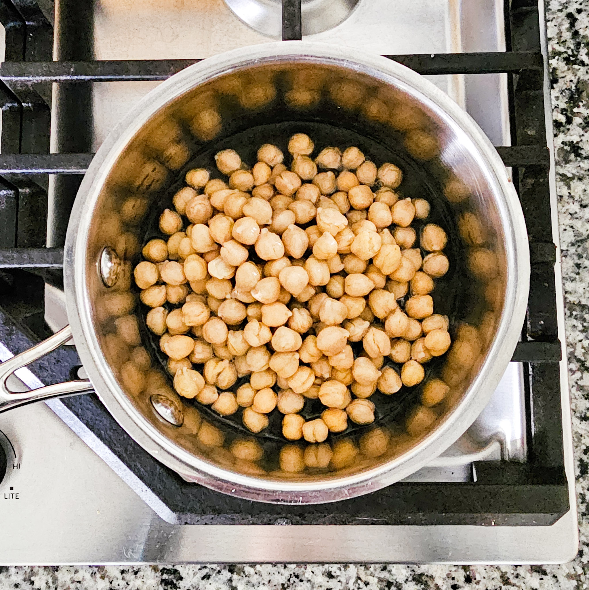Chickpeas needed to make gluten-free vegan creamy musabaha in a stainless-steel saucepan on a gas cooktop.