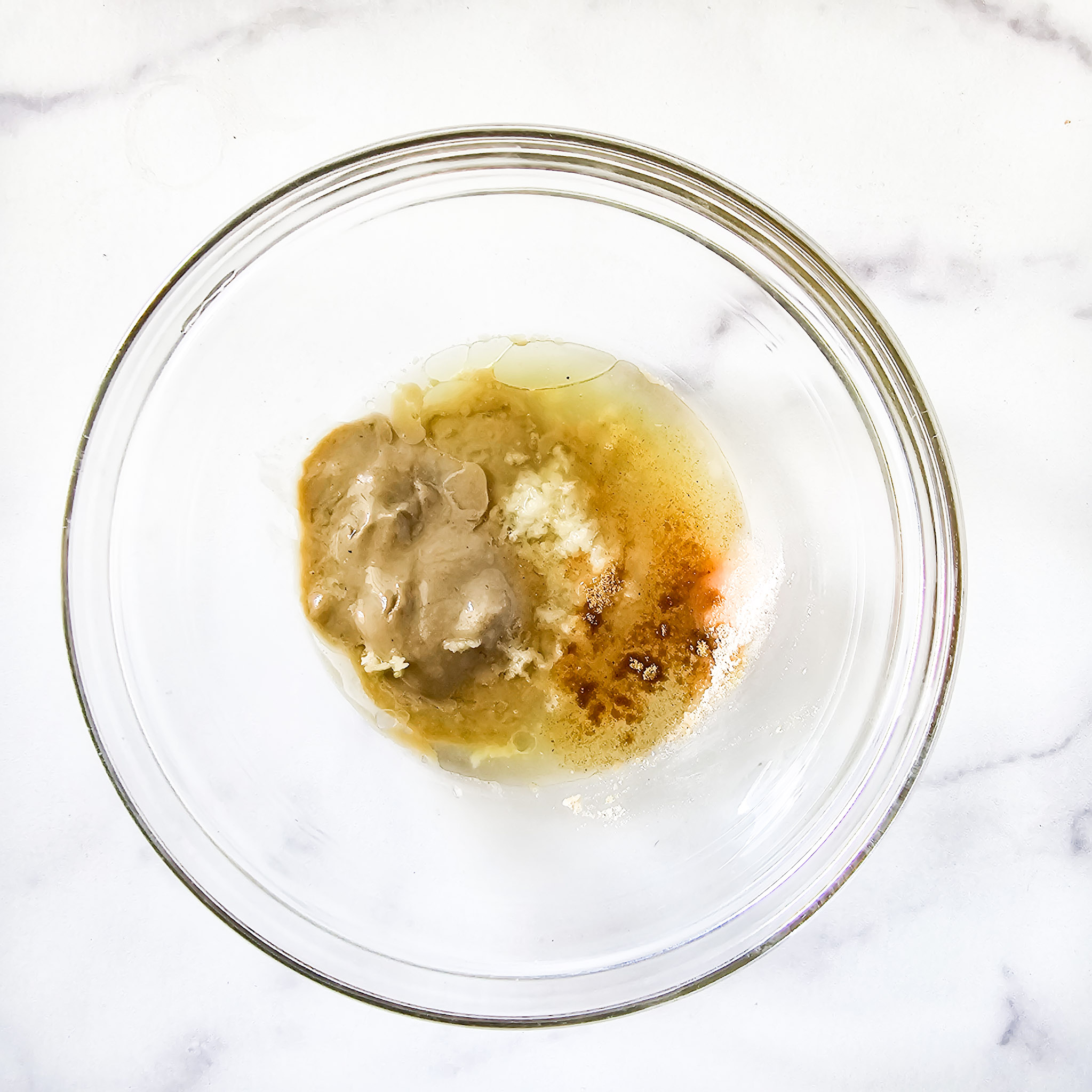 Overhead image of ingredients needed to make gluten-free vegan creamy musabaha tahini sauce in a glass bowl on a white marble surface.