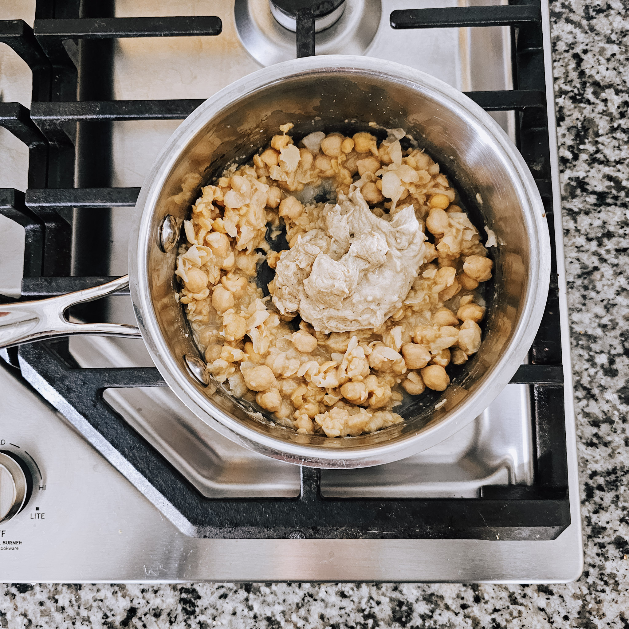 Overhead image of the ingredients to make gluten-free vegan creamy musabaha in a stainless-steel saucepan on a gas cooktop.