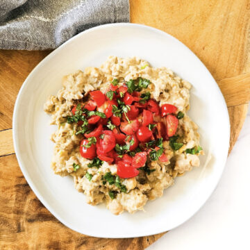 Overhead image of gluten-free vegan creamy musabaha on a white plate on a wooden surface on a white background.