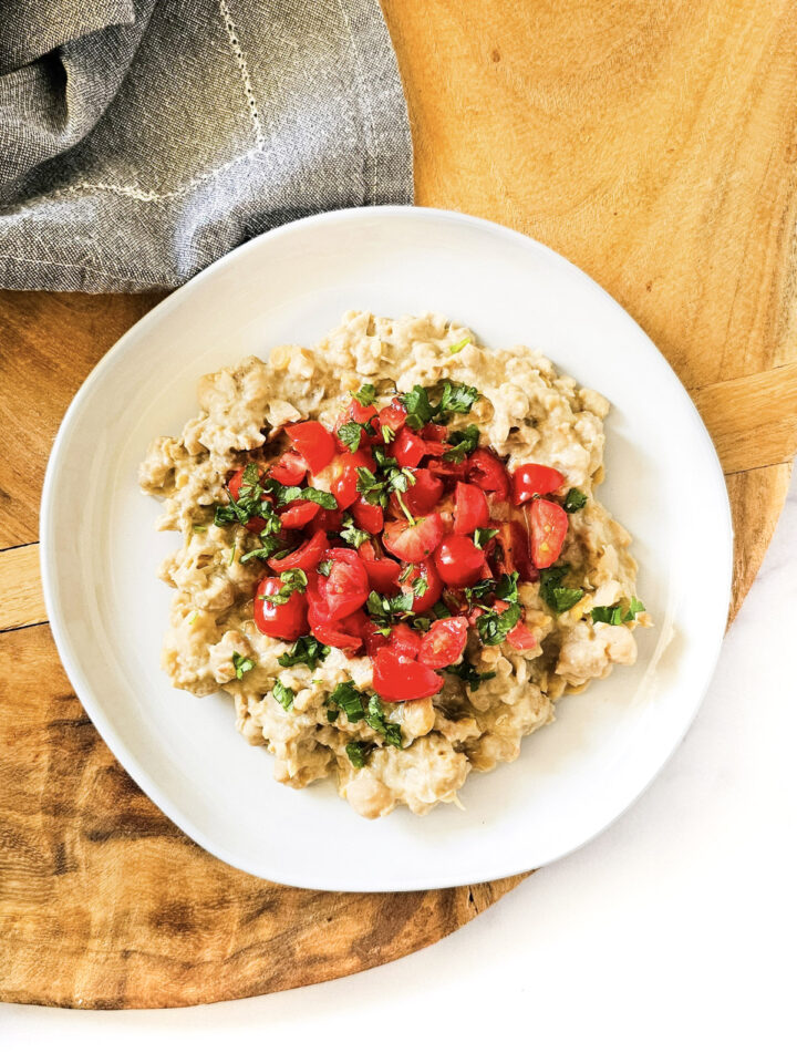 Overhead image of gluten-free vegan creamy musabaha on a white plate on a wooden surface on a white background.
