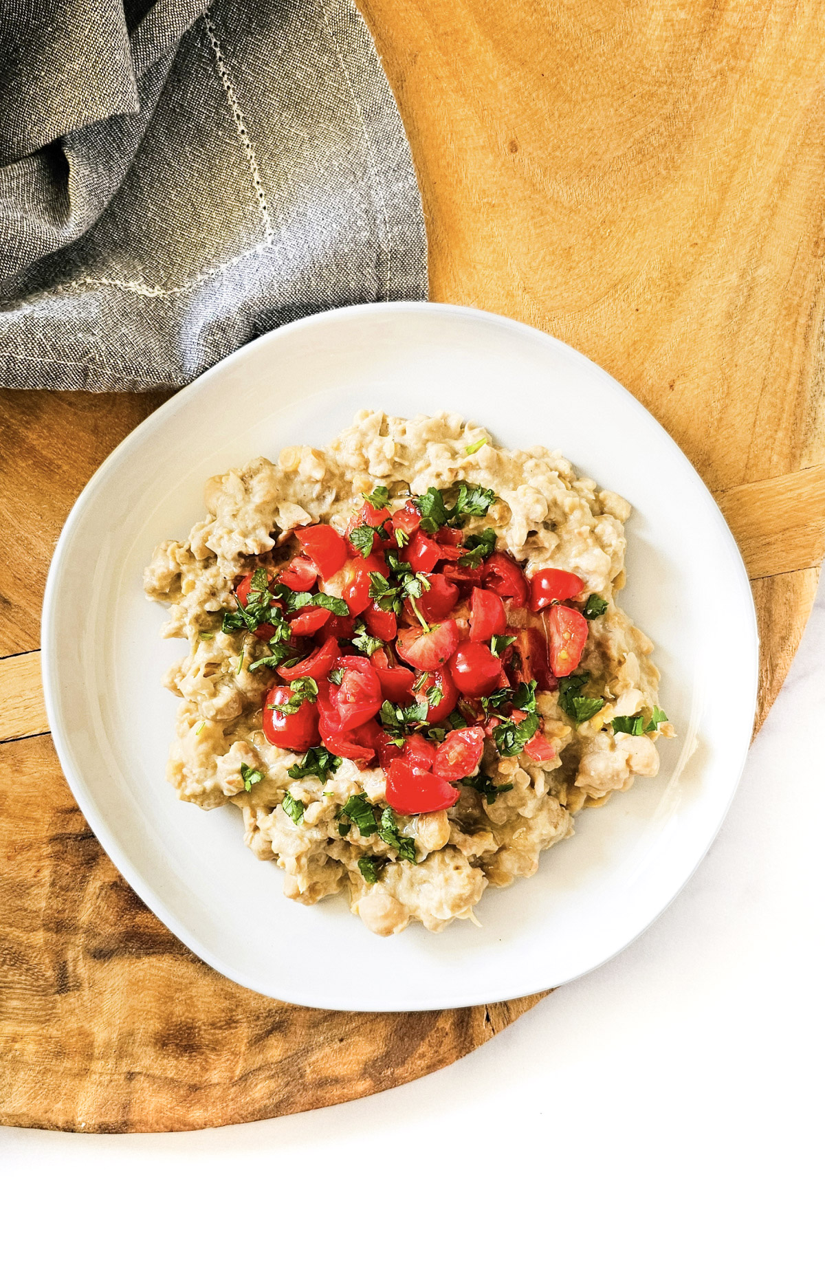 Overhead image of gluten-free vegan creamy musabaha on a white plate on a wooden surface on a white background.