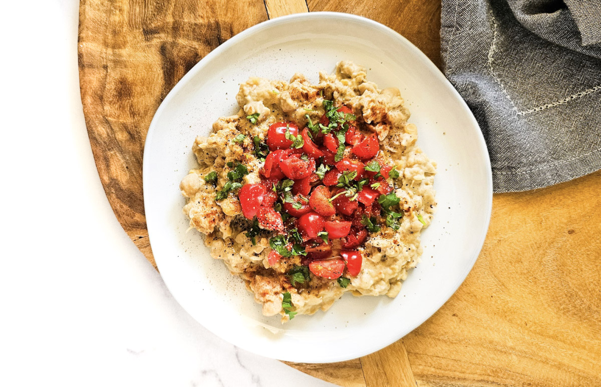 Overhead image of gluten-free vegan creamy musabaha on a white plate on a wooden board on a white marble surface.